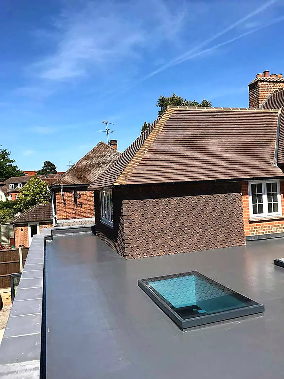 A grey fibreglass flat roof with a rooflight, tiled house behind