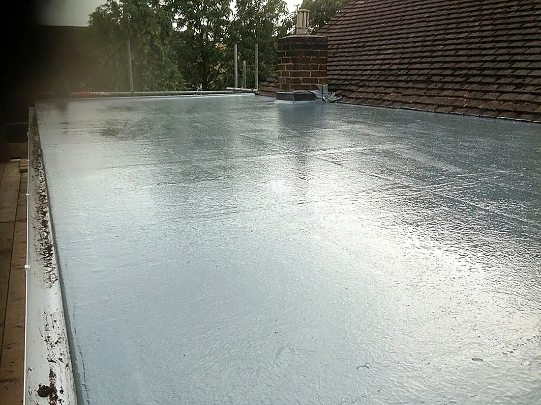 A fibreglass flat roof wet after rain, with a tiled roof behind