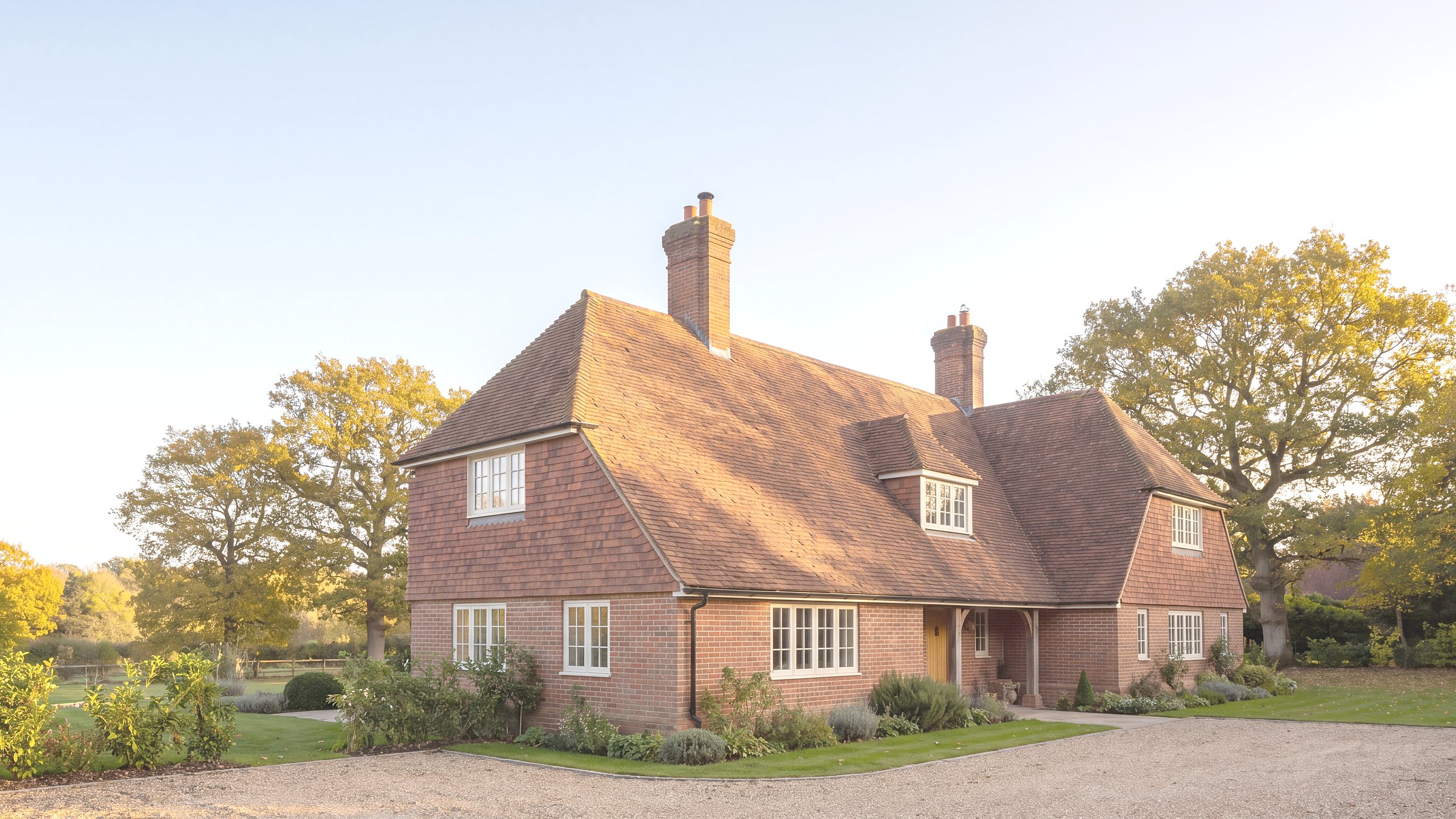 A detached English house with a clay tiled roof and brick chimney stacks, lit by low golden evening sun