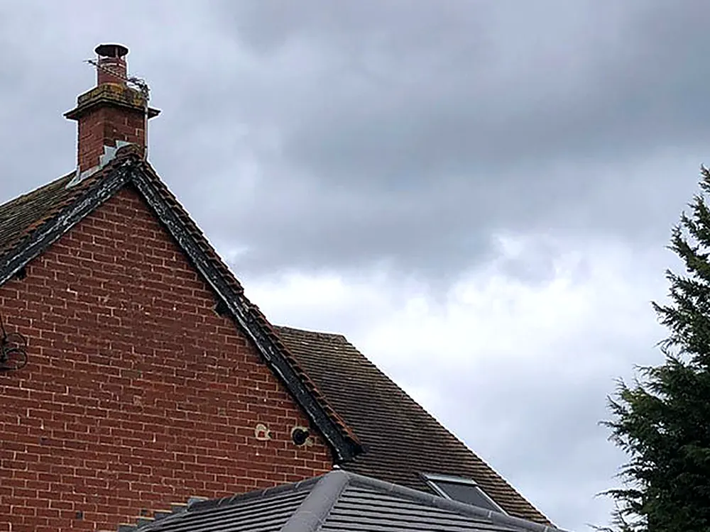 A brick chimney stack on a tiled gable under a grey sky