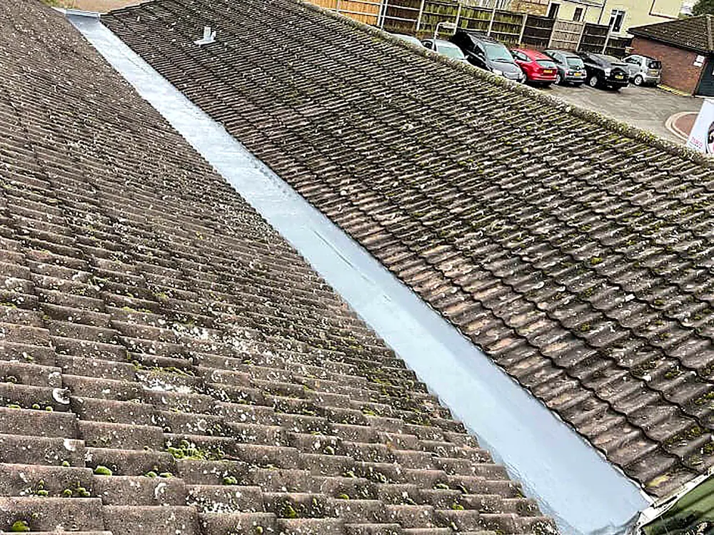 An older tiled roof with a newly lined valley among the mossy tiles